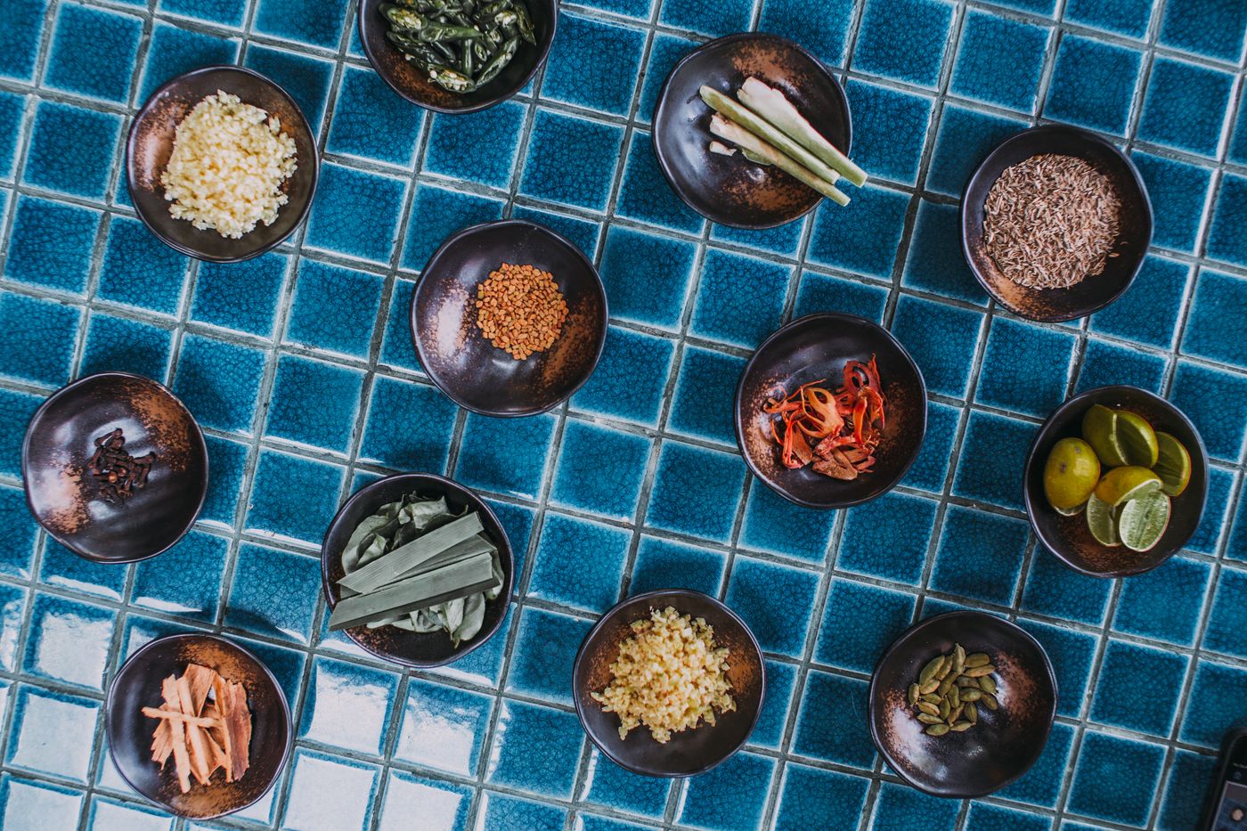 Whole spices and aromatic ingredients in bowls on blue tiles