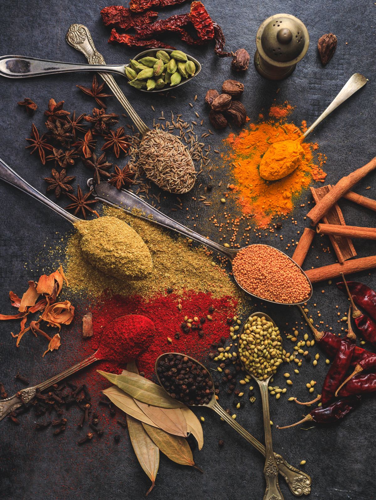 Turmeric, chilli powder, cumin and whole spices arranged on a dark surface